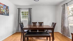 Een eetkamer met een houten tafel en stoelen, een bank, gordijnen met een patroon, en een raam met uitzicht.