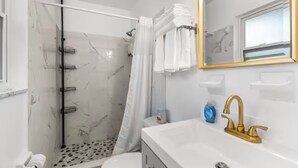 Een badkamer met douche, toilet, wastafel en een spiegel met gouden lijst.