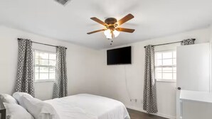 Een slaapkamer met een bed, een plafondventilator, een televisie en kamer met patroon gordijnen.