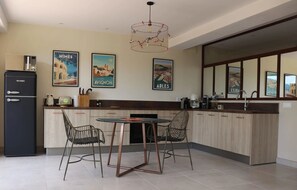 Una cocina con un refrigerador negro, dos sillas, una mesa redonda y una lámpara colgante.