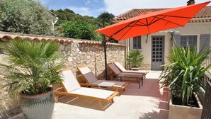 A sunlit patio with lounge chairs and a red umbrella, surrounded by stone walls and potted plants. - Les Terrasses de la Roque Alric (La Roque-Alric)