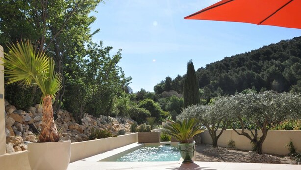 A pool area with a stone wall, potted plants, and a view of a forested hillside. - Les Terrasses de la Roque Alric (La Roque-Alric)