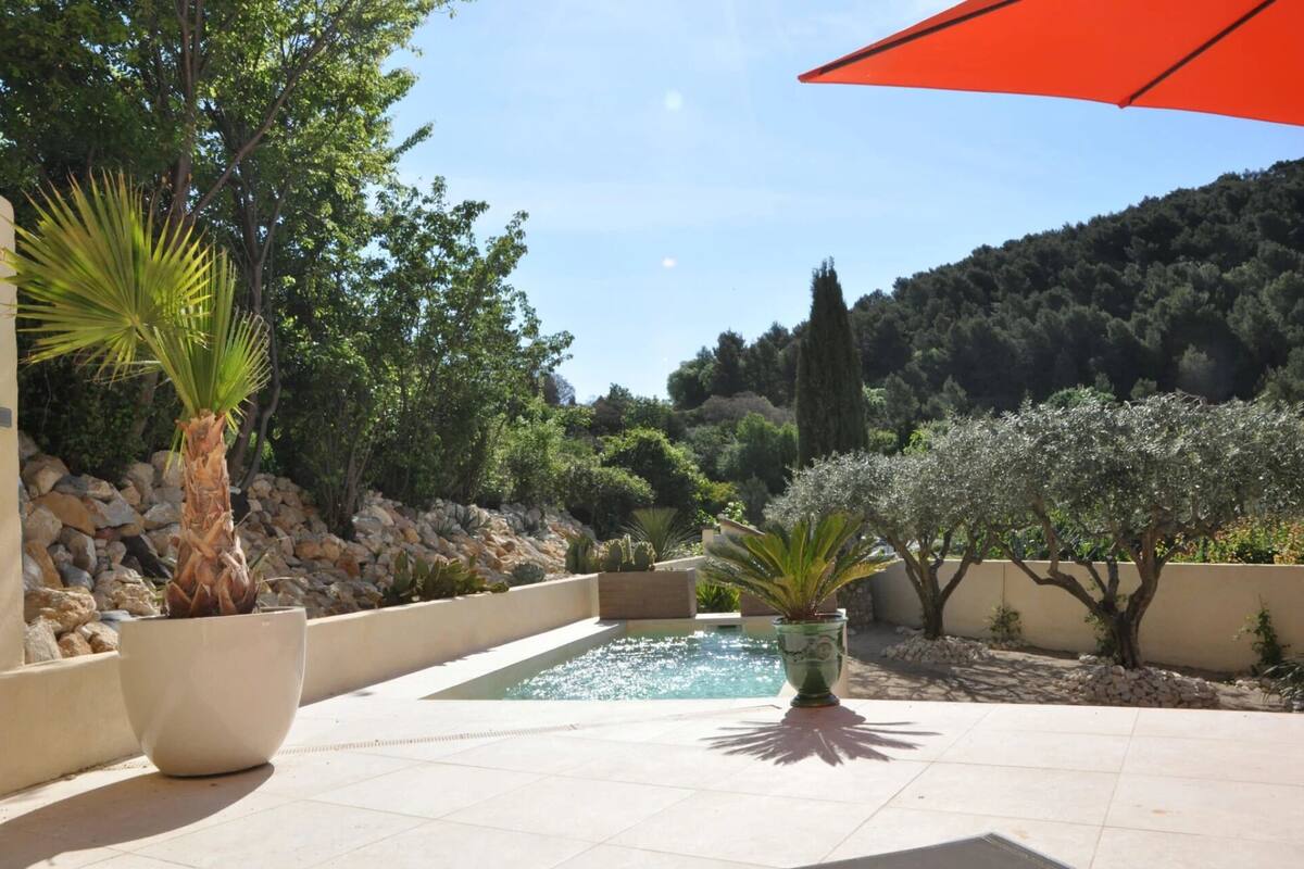 A pool area with a stone wall, potted plants, and a view of a forested hillside.