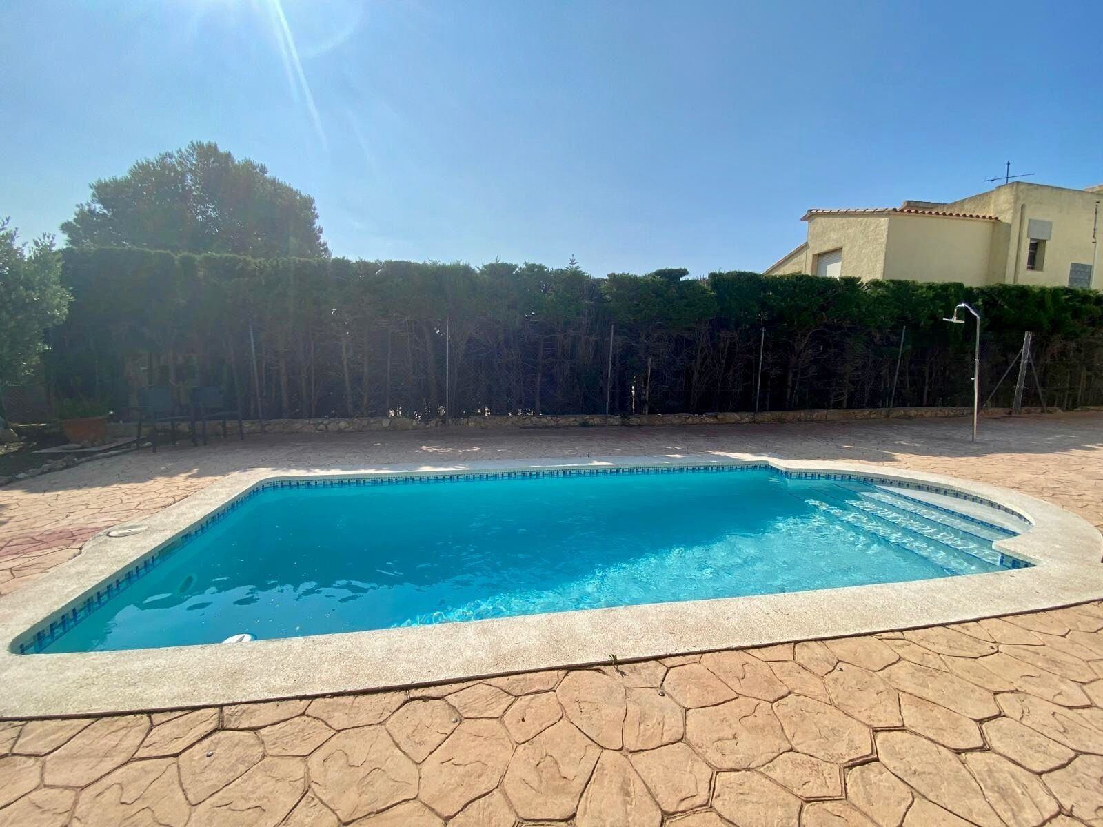 A rectangular swimming pool with a tiled edge, surrounded by a hexagonal stone patio.