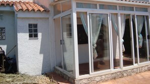 Una casa con una sala de estar iluminada por el sol, con grandes puertas de vidrio y techo de tejas.