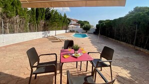 Un patio con mesa y sillas, piscina y vistas a una casa y árboles.