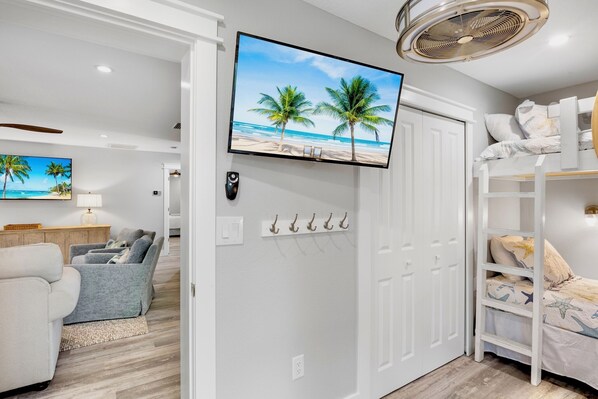 A room with a TV mounted on a white door, a bunk bed with a beach-themed bedspread, and a seating area with a sofa and armchairs.