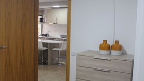 A bedroom with a bed, a wooden wardrobe, and a kitchenette in the background. - Your retreat between turquoise shores and forested paths (Machico)