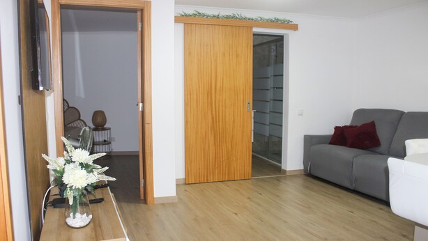 A living room with a grey sofa, a wooden cabinet, and a TV mounted on the wall. - Your retreat between turquoise shores and forested paths (Machico)