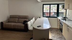 A modern kitchen with a central island, a sofa, and a window with a city view. - Your retreat between turquoise shores and forested paths (Machico)