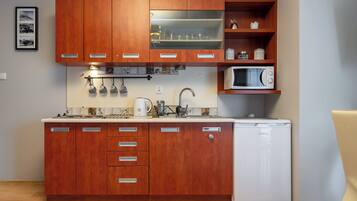 Een kleine keuken met houten kastjes, een magnetron, een koffiezetapparaat en een koelkast.