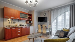 Una sala de estar moderna con un sofá, una mesa de centro y un televisor. Hay una zona de cocina con armarios de madera y un microondas.