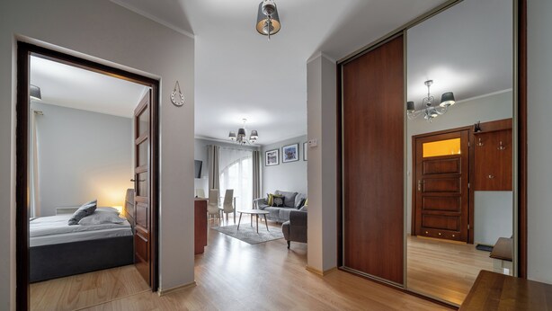 Una sala moderna con sofá, mesa de centro y comedor con sillas. El piso es de madera y hay un espejo grande que refleja la habitación.