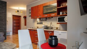 Una cocina moderna con armarios de madera, un microondas y un comedor con mesa de vidrio y sillas blancas.