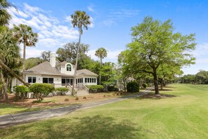 A single-story house with a porch, surrounded by a well-maintained lawn and trees. - Seabrook SEArenity, Pet/Family Friendly 5bd/4.5bath, Golf course views, golf cart available (Seabrook Island)