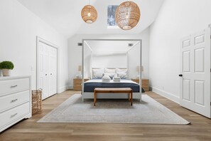Un dormitorio con cama con dosel, paredes blancas, suelo de madera y dos lámparas colgantes de mimbre.