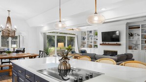 A modern kitchen with a central island, pendant lights, and a dining area with wicker furniture.