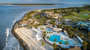 A coastal resort with a large pool, beachfront seating, and multiple buildings.