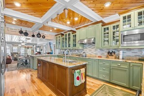 A kitchen with wooden ceiling beams, green cabinets, and a central island with a sink.