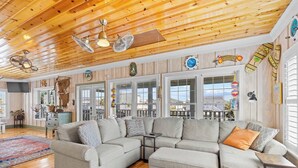 A spacious living room with a large sectional sofa, wooden ceiling, and large windows offering a view of the outside. - A Lady's Place (North Myrtle Beach)