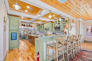 Una cocina con vigas de madera en el techo, armarios verdes y una isla central con taburetes de bar.