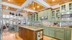 A spacious kitchen with wooden ceiling beams, green cabinets, and a central island with a sink. - A Lady's Place (North Myrtle Beach)