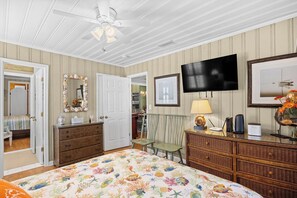 A bedroom with a bed, dresser, television, and framed pictures.