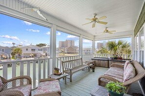A covered outdoor area with a wooden deck, wicker furniture, and a view of buildings in the distance.