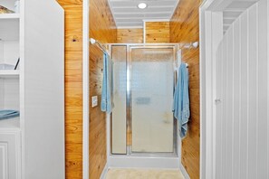 Una ducha con puertas de vidrio esmerilado, paneles de madera en las paredes y una puerta blanca a la derecha.