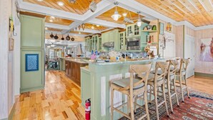 A spacious kitchen with wooden beams, green cabinets, a central island with bar stools, and a large island sink. - A Lady's Place (North Myrtle Beach)