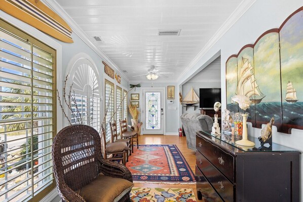 A room with a large window, a wicker chair, a patterned rug, and a television on a stand.