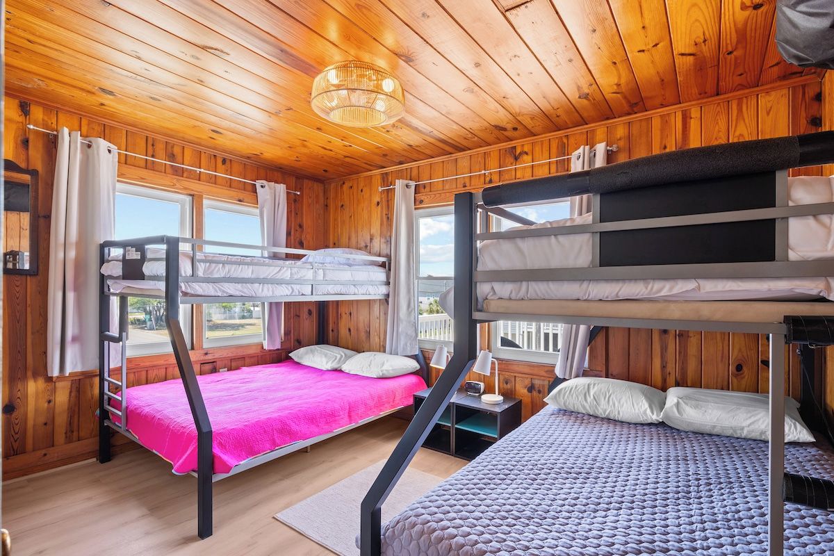 A cabin with wooden walls and ceilings, bunk beds, a window, and a nightstand.