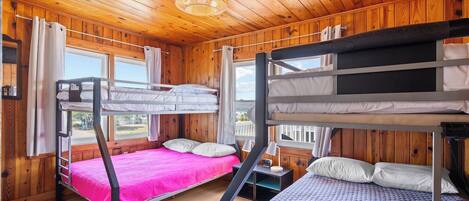 A cabin with wooden walls and ceilings, bunk beds, a window, and a nightstand.