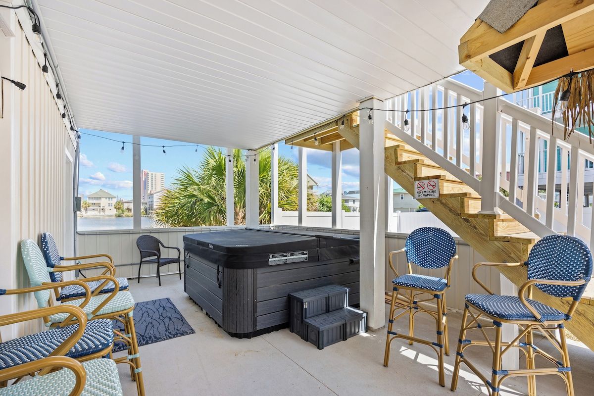 A covered outdoor area with a hot tub, seating, and a staircase.
