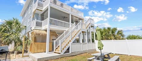 A two-story house with a balcony, a staircase, and a patio area with a table and chairs.