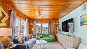 A cozy living room with a wooden ceiling, a green sofa, a blue couch, and a flat-screen TV.