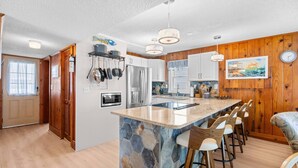A modern kitchen with a central island, bar stools, and a stone backsplash.
