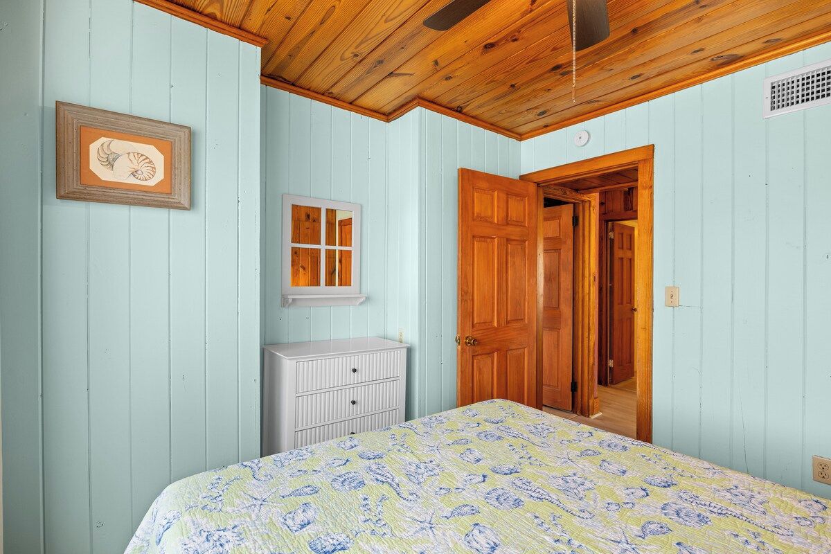 A bedroom with a bed, a dresser, a wooden door, and a framed picture on the wall.