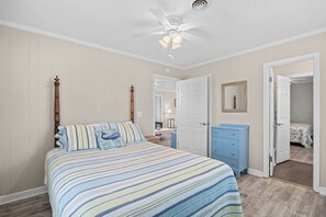 Ein Schlafzimmer mit einem Bett, einer Kommode, einem Deckenventilator und einer Tür zu einem anderen Raum.