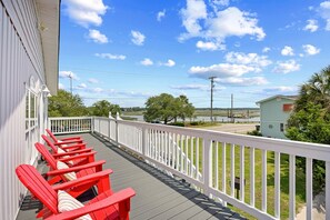 Une terrasse avec des chaises rouges et une balustrade blanche, donnant sur une étendue d’eau et une zone verdoyante.
