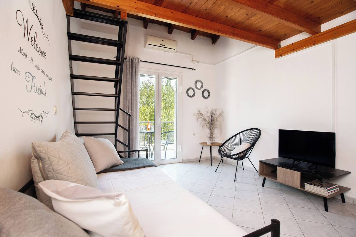 A modern living room with a sofa, a TV, a staircase, and a view of the outdoors.