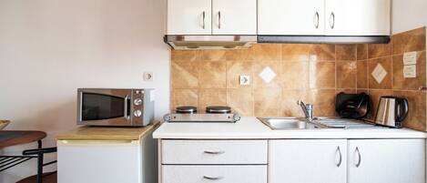A compact kitchen with white cabinets, a microwave, a stove, and a sink.
