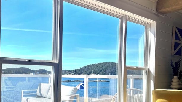 Ett rum med stora fönster som vetter mot en terrass med utomhusmöbler och utsikt över havet.