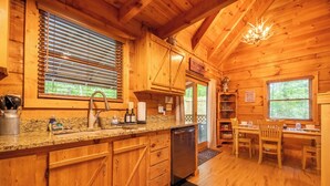 Ein Holzblockhaus-Innenraum mit einer Küche, die ein Spülbecken, einen Herd und einen Kühlschrank umfasst. Es gibt einen Essbereich mit einem Tisch und Stühlen.
