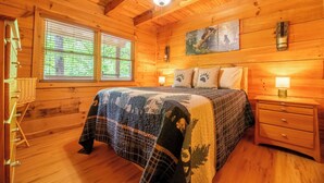 Ein gemütliches Schlafzimmer in einer Holzhütte mit Bett, Nachttischen und Deckenventilator.