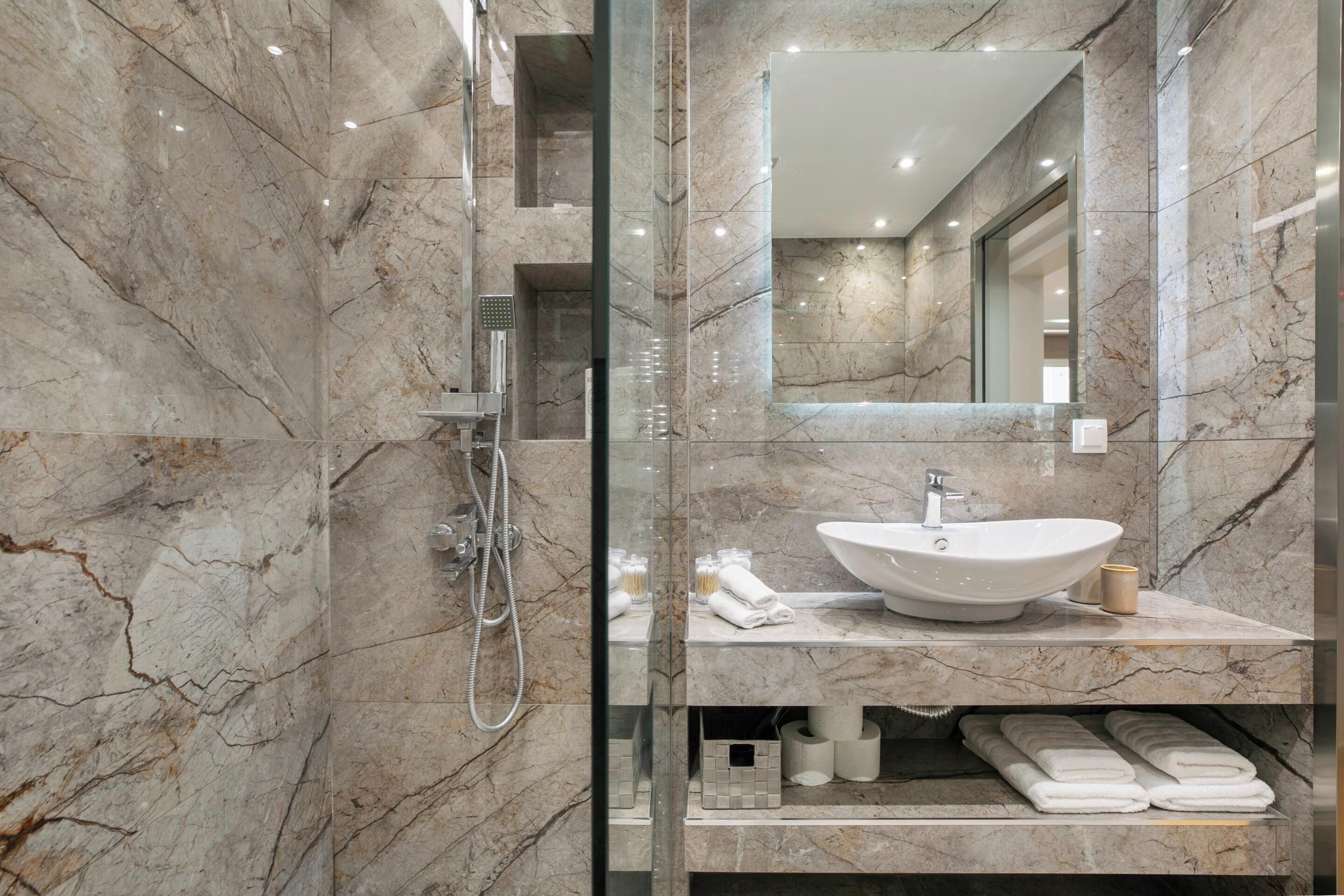 A modern bathroom with a marble sink, glass shower enclosure, and a large mirror.
