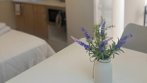 A room with a bed, a small table with a vase of flowers, a kitchenette with a refrigerator, and a window. - Studio Apartment 'Episkopos' with Private Terrace, Wi-Fi and Air Conditioning (Lefkada)