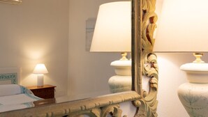A mirror with ornate carvings, a bed with a blue headboard, and two bedside lamps. - Casa Acqua e Pietra by Wonderful Italy (Golfo Aranci)