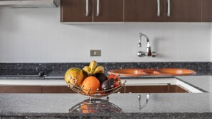 A kitchen with a fruit bowl on the counter, a sink, and wooden cabinets.