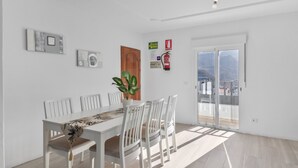 A dining area with a white table and chairs, a potted plant, and a view through a glass door.